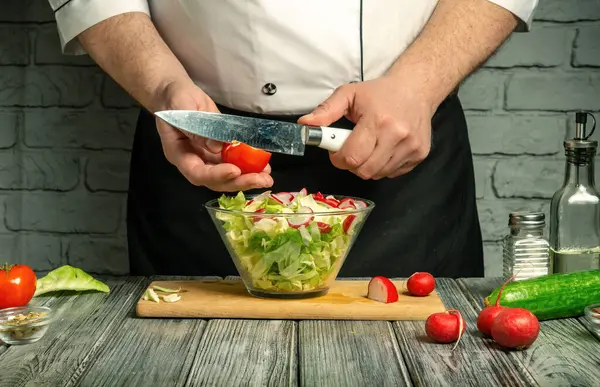 Bir şef sıcak bir mutfakta renkli bir salata hazırlarken domates ve turpları ustaca doğruyor. Taze sebzeler karıştırılmaya hazır cam bir kasenin etrafına dizilir..