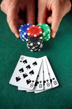 İki el renkli poker fişlerini kavrarken, iki sekizli ve iki onlu kağıt bir kart oyunu sırasında yeşil bir keçeli masa üzerinde duruyor..