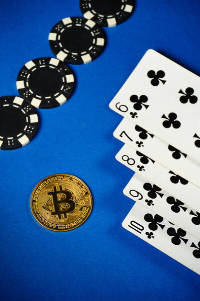 Poker cards straight flush and black chips lay next to a shiny bitcoin on a blue surface. This setup reflects an exciting gambling scene involving cryptocurrency.