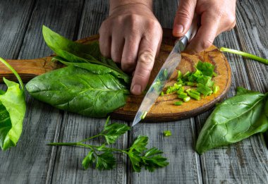 Elleri ustalıkla taze ıspanak ve otları tahtadan kesme tahtasında doğruyor, besleyici bir yemek için malzemeleri hazırlıyor. Sahne, yemek pişirmenin ve sağlıklı beslenmenin özünü yakalıyor..