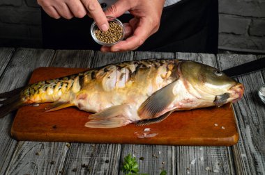 Bir şef bütün balığı baharatlarla tatlandırıyor, balığın üzerine küçük bir kap baharat koyuyor. Köy mutfağı ahşap elementler ve basit dekorlarla dolu..