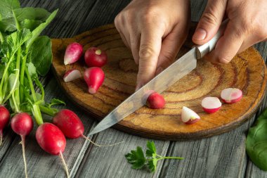 Kırsal bir tahtanın üzerinde canlı turpları kesen eller. Kesim bölgesini çevreleyen taze yeşiller ev mutfağında basit bir yemek hazırlığı sergiliyor..