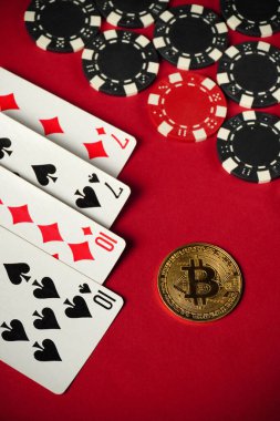 Bir çift onluğu ve yediyi gösteren kartlar, yakınlarda dağılmış, parlak kırmızı bir masanın üzerinde, dijital para birimini sembolize eden siyah ve beyaz poker çipleri ve parlak Bitcoin 'ler bulunuyor..