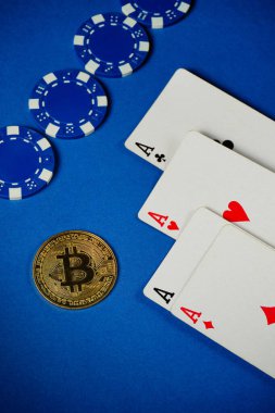 Three playing cards showing aces and a pair of chips are arranged neatly next to a Bitcoin coin on a blue surface, creating a vibrant casino scene.