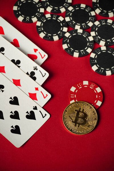 Four of a kind or quads playing cards are laid out next to black and red poker chips. A shiny Bitcoin coin lies nearby, evoking the atmosphere of modern gambling.