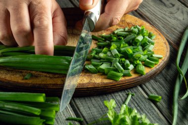 Hands skillfully chop bright green onions and fresh herbs on a wooden board. The kitchen atmosphere feels warm and inviting, perfect for cooking.