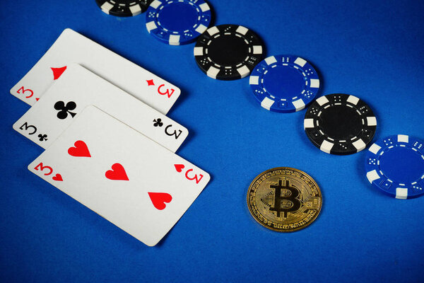 The game scene features three playing cards depicting three of a kind or set surrounded by black and blue poker chips, as well as a Bitcoin coin prominently displayed on a blue table.