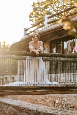 Güzel gelin gün batımında bir nehrin üzerindeki ahşap kırsal köprüde duruyor.