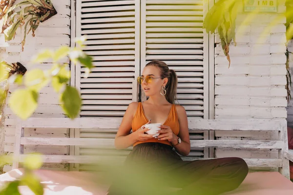주황색 안경을 티셔츠를 야외에서 커피를 마시며 이국적 금발의 여성을 — 스톡 사진