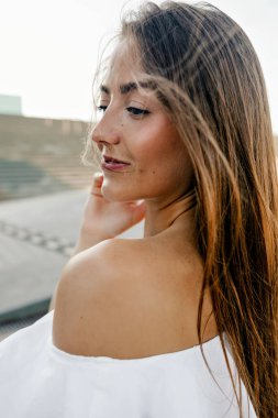 Kapalı profil portresi, beyaz elbiseli, açık havada gülümseyen, çıplak omuzlu, çekici, güzel bir kadın. 