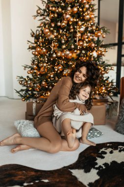 Uzun, mutlu, bukleli, süveter giyen ve Noel ağacının yanında eğlenen genç bir kadının fotoğrafı.. 