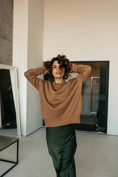 魅力的なスリムスタイリッシュな女性とともに波状の髪身に着けている茶色のセーターとシルクスカートポーズでカメラインスタジオ — ストック写真