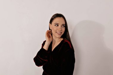 Koyu renk elbiseli, büyüleyici genç bir kadın harika bir gülümseme ve makyajla yan yana bakıyor. Koyu saçlı kız geniş bir şekilde gülümser. Kutlama kavramı, kopyalama alanı.