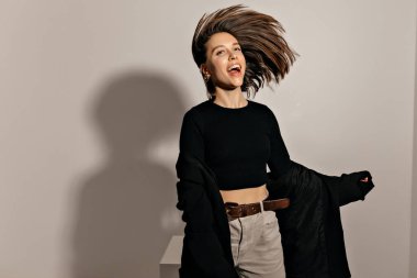 Uçan saçlarıyla, koyu renk ceketi ve gömleğiyle mutlu ve mutlu bir kız izole bir arka planda dans ediyor.. 