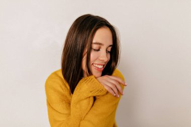 Siyah saçlı, harika bir gülümsemesi olan sarı örgü süveter giyen mutlu bir gülümsemeyle aşağıya bakan romantik bir kızın yakın portresi..