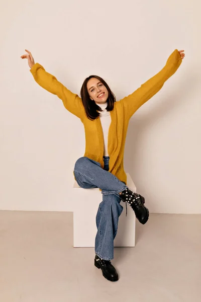 イエローのシャツとジーンズを着た黒髪の可愛いエネルギーの女の子のフルレンズ写真が独立した背景に手を挙げて椅子に座って — ストック写真