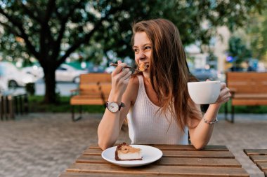 Hafif yaz kıyafetleri giyerek, kahve içerek, tatlı yiyerek ve yazlık kafede dinlenirken yan tarafa bakarak mutlu, sevimli, çekici bir his. 