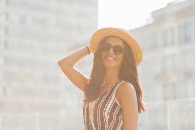 Cheerful glad lady in summer suit and hat and sunglasses smiles and having fun in the city on sunset. Recreation, weekend, walking in the city 