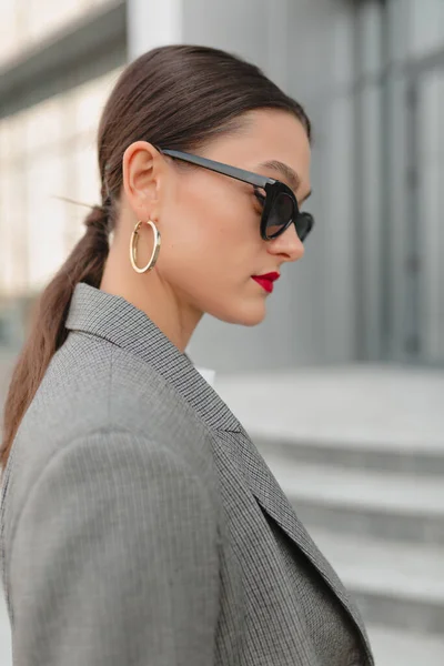 Close up profile portrait of charming cute woman with dark hair and red lips in dark glasses posing outdoor while walking in the city