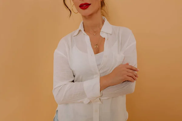 ベージュ地の上に腰に十字型の腕を背負った白いシャツを着た赤い唇を持つスタイリッシュなかわいい女の子のクロップ写真 美の概念 — ストック写真