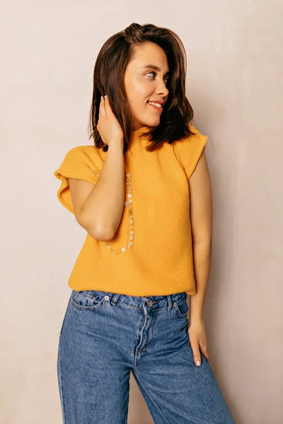 穿着黄色T恤 牛仔裤在米色背景的衬托下 是一位可爱的女士 拥有时髦的短发风格 生活方式 不同的情感 休闲观念 — 图库照片