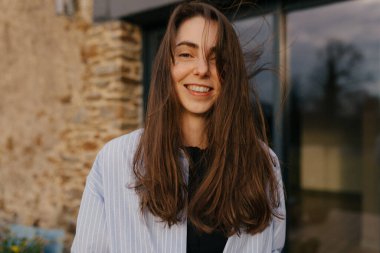 Açık renk tişört giyen mutlu, heyecanlı kadın, gün ışığında terasta eski taş evin karşısında kameraya gülüyor. Rahatla konsept