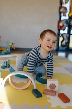 Çizgili gömlekli ve pantolonlu küçük bir çocuk çocuk çocuk halısında tahta oyuncaklarla oynuyor. Çocukların tahta oyuncakları. Ayırıcı. Çocuk gelişimi için Montessori.