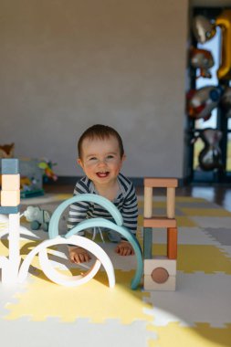 Güneş ışığındaki sevimli sevimli küçük çocuğun yakın plan portresi kameraya gülümsüyor ve eğitici tahta oyuncakların tadını çıkarıyor. Küçük çocuk ahşap elementlerle inşa ediyor.