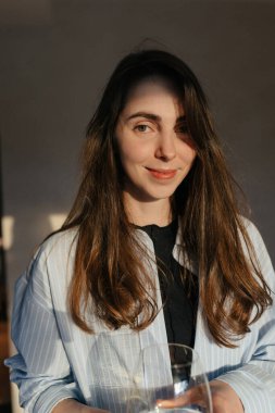 Kapalı mekanda gülümseyen esmer kadının portresi güneş ışığında izole edilmiş arka planda kameraya poz veren bir bardak tutuyor. Güzel konsept 