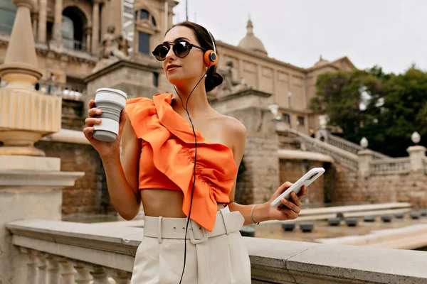 Kulaklıklı Çekici Avrupalı Bayan Öğrenci Telefonuyla Kameraya Bakıyor Parlak Turuncu — Stok fotoğraf