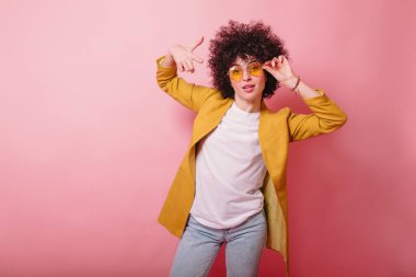  Pembe arka planda izole edilmiş sarı ceketli manken portresi ve barış işareti. Güzellik, sanat, moda, gençlik, satış ve reklamlar. Güzel kadın poz veriyor