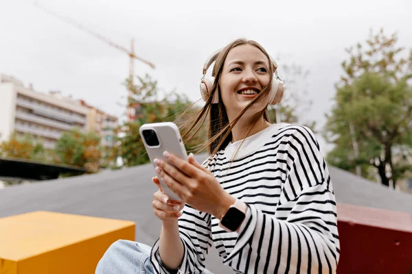 Açık havada çekilen güzel kızların açık havada çekilmiş fotoğrafları bol saçlı, çizgili tişörtlü kızlar akıllı telefon kullanıyor ve dışarıda müzik dinliyor.. 