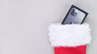 iPhone hediye kutusu Noel çoraplarından dışarı bakıyor. Noel Baba 'nın hediyelerle dolu kırmızı çorabı. Noel ya da tatil kavramı. Gri arka planda hediyeler. Gatineau, QC Canada - 21-12-2022