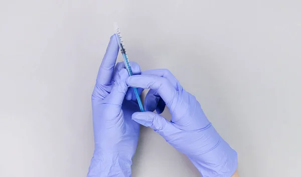 Hands in blue gloves of doctor or nurse holding syringe with liquid vaccine over grey background with copy space. New vaccine. Unknown vaccine. Medical gloves