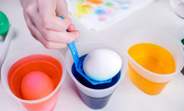 Kid hand paints eggs for easter holidays. Dyeing easter eggs at home. Child creates festive decorations.