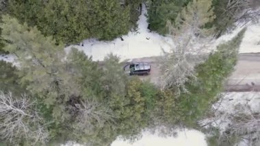 Aerial view of mountain twisted road in the winter and driving car. Snowy white winter and snow forest. Road through frozen forest and luxury sedan driving. Winter road trip