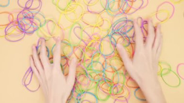 Hands taking bunch of colorful rubber bands on yellow background. Bright office rubber bands. Multicolored elastic rubber bands close up