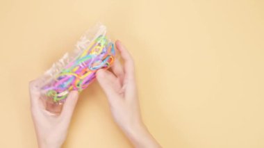 Hands opened small plastic bag with bunch of colorful rubber bands and por them out on yellow background. Bright office rubber bands. Multicolored elastic rubber bands close up