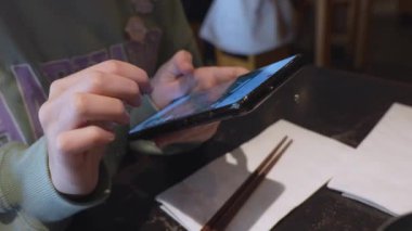 Hand of girl using texting mobile phone or chat while waiting food at restaurant. Close up of woman hand.