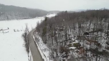 Aerial view of mountain twisted road in the winter and driving car. Snowy white winter and snow forest. Road through frozen forest and luxury sedan driving. Winter road trip