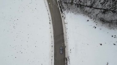 Aerial view of mountain twisted road in the winter and driving car. Snowy white winter and snow forest. Road through frozen forest and luxury sedan driving. Winter road trip.