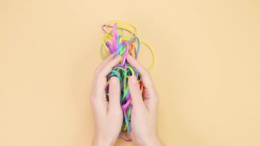 Hands taking bunch of colorful rubber bands and squizzing them on yellow background. Bright office rubber bands. Multicolored elastic rubber bands close up.