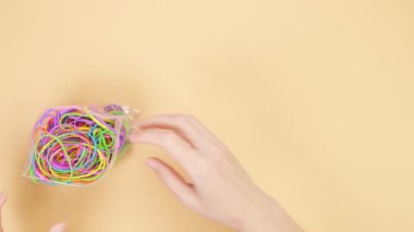 Hands taking colorful rubber bands out of small plastic bag and put them on yellow background. Bright office rubber bands. Multicolored elastic rubber bands close up.