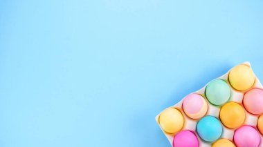 Colorful Easter eggs pack on blue background with space for text. Minimal spring flat lay. Pastel painted eggs in box