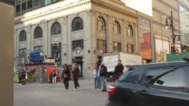 People crossing the road on busy street in Montreal. Rush hour traffic. Cars passing through. People walking along street exploring the city. Sunny day. Montreal, QC Canada 10.22.2022