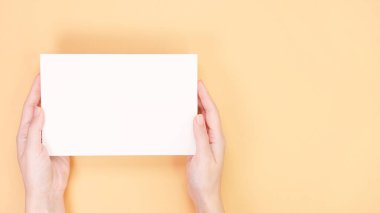 Açık sarı arka planda genç bir kadının elinde mesaj ve tasarım için boş yeri olan beyaz model kart. Tahta, boş, şablon, model, slogan için düzen