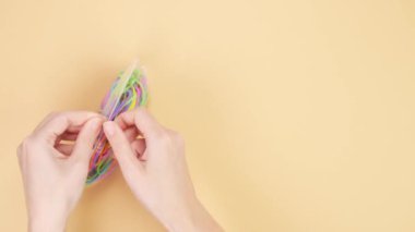 Eller sarı arka planda renkli lastik bantlarla dolu küçük plastik torbaları açtı. Parlak ofis lastikleri. Çok renkli lastik bantlar kapanıyor.
