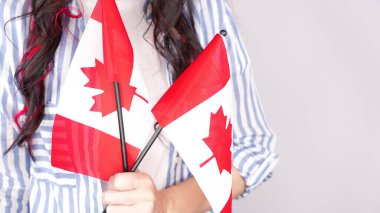 Gri arka planda küçük Kanada bayrağı taşıyan beyaz tişörtlü tanınmamış kız çocuğu, Kanada günü, tatil, oy, göç, vergi, kopya alanı.