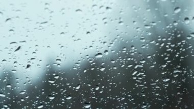 Snow fall on window and melting into water drops on glass in the forest. Large rain drops strike window during winter shower. Pure rain drops