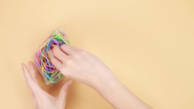 Eller sarı arka planda renkli lastik bantlarla dolu küçük plastik torbaları açtı. Parlak ofis lastikleri. Çok renkli lastik bantlar kapanıyor.